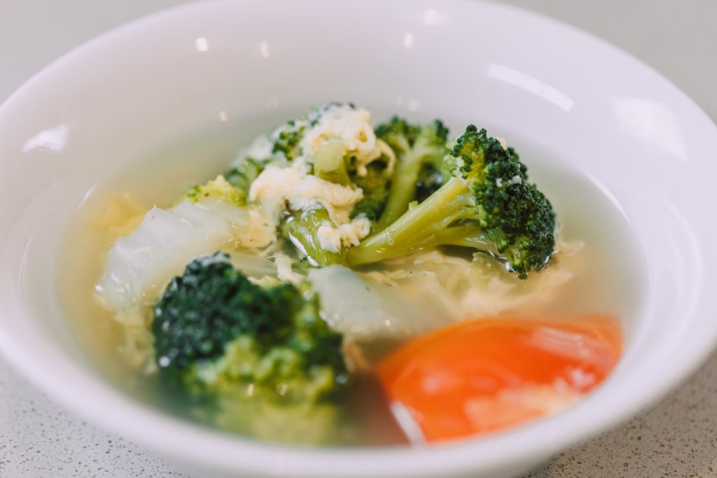 A bowl of soup and broccoli on a plate